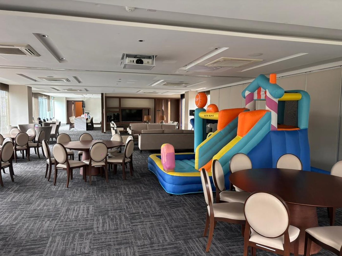 Inflatable bouncy castle with a slide set up inside a hotel function room next to round dining tables and chairs
