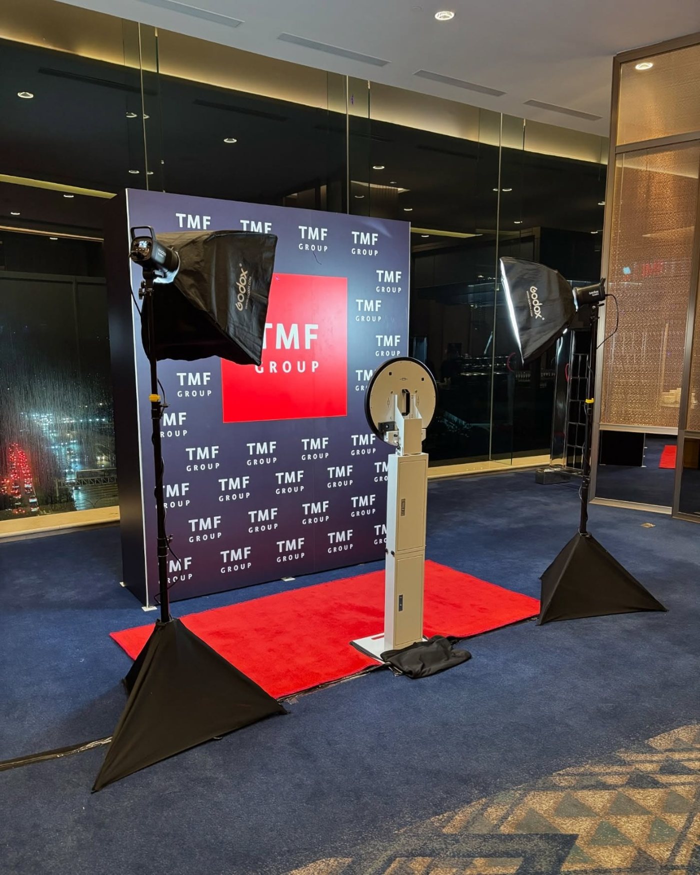 Digital photo booth and two softbox lights in front of a corporate step-and-repeat banner with a red carpet runner