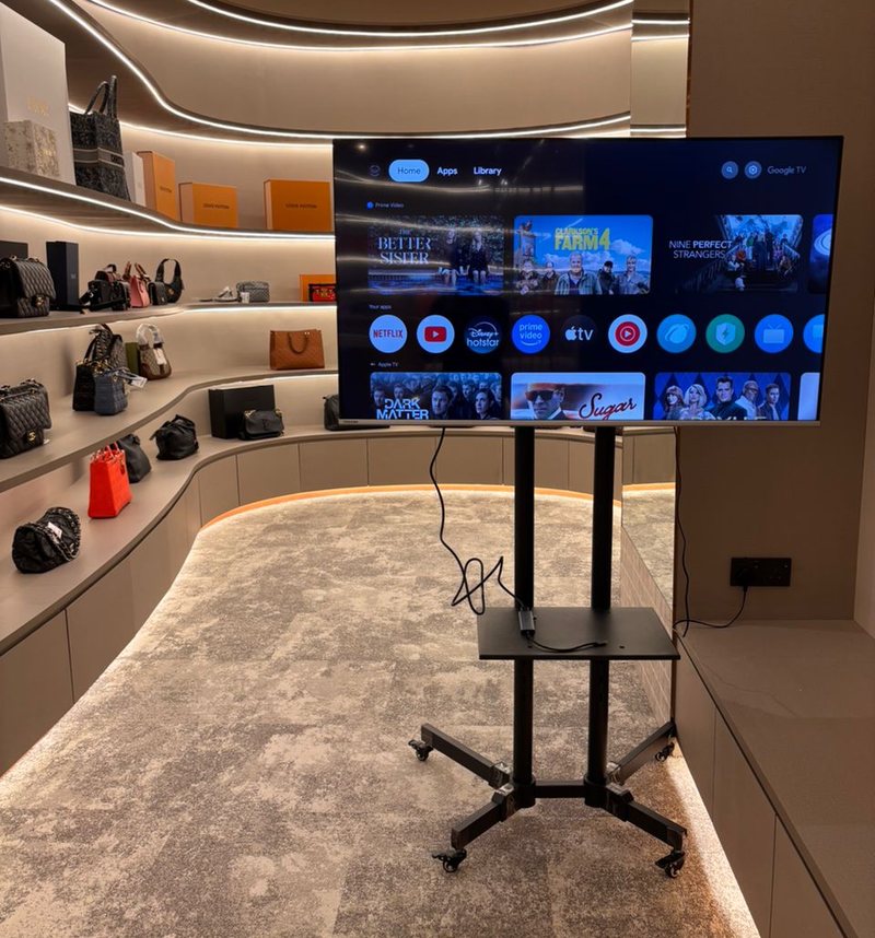 50-inch LED TV on a black wheeled floor stand inside a retail showroom, screen showing a smart TV home menu