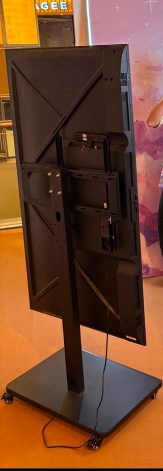 Rear view of a 65-inch LED TV mounted in portrait orientation on a wheeled floor stand