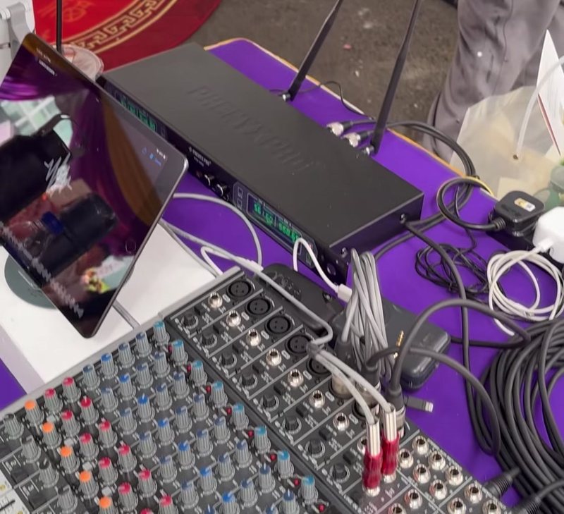 Close view of an analogue mixing desk and rack-mounted wireless microphone receivers on a table at an outdoor event